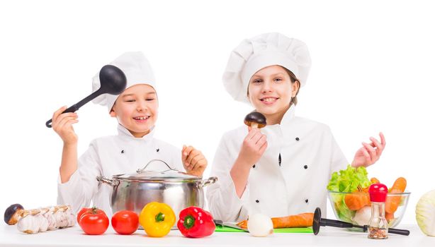 little boy and girl in white uniform with vegetables for soup on kitchen table