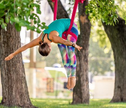 Girl during fly yoga in hammock stretching at nature and keeping balance in the air. Young woman doing aero fitness gymnastic exercising outdoors
