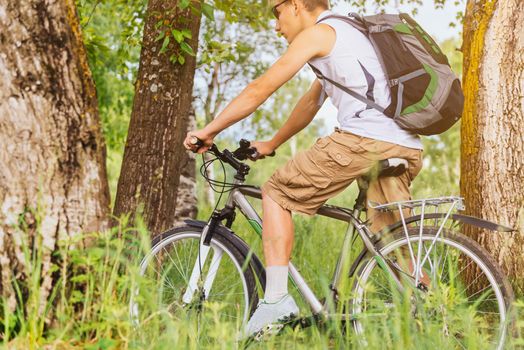 Cyclist man with backpack riding mountain bike in summer forest, theme of sport and hiking