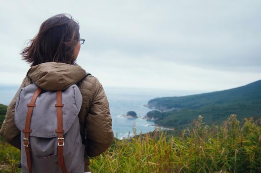 Hiker young woman with backpack looking into distance to the island in a blue sea