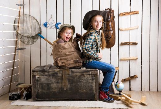 cute little girl with another little girl in backpack sitting on big wooden chest