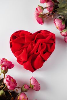 Red heart shaped gift box and flowers on white background. Festive design - red heart surrounded by delicate pink flowers on a white background, vertical photo.