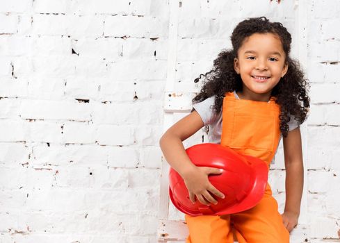 pretty little girl in repairman uniform with helmet in hands sitting on ladder