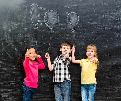 three smiling children with thumbs up keeping imaginaru drawn balloons on a chalky blackboard