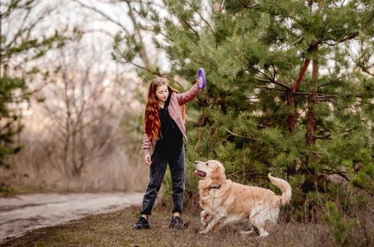 Girl teenager training golden retriever dog in the wood using rubber ring