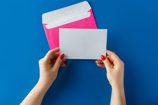 Pink envelope with a blank card in hands on a blue background. Hands holding a pink envelope with a blank letter on a blue background.