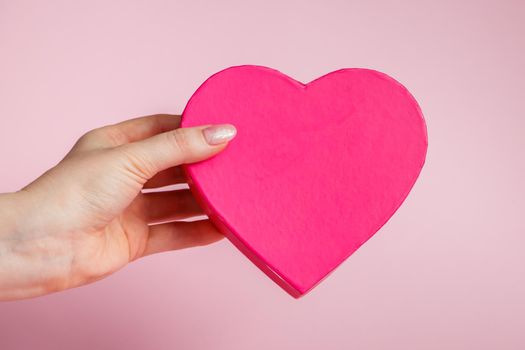 Big pink heart-shaped box in hand on a light background. Giving a gift for Valentine's Day. Place for text.