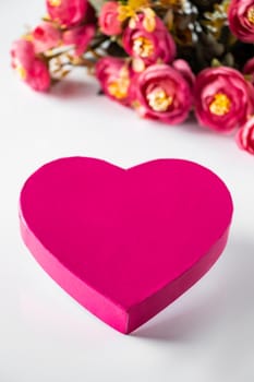 Pink heart for valentines day on a background of flowers. Close-up pink heart and a bouquet of flowers on a white background. Place for text, vertical photo.