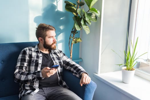 Technologies and leisure concept - Cheerful man sitting on the couch using his smartphone at home in living room.