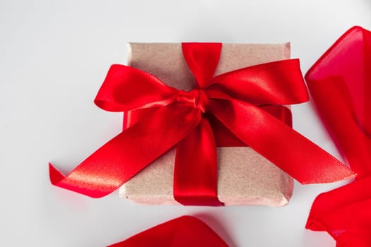 Gift box with craft paper and red ribbon on a white background. Beautiful gift box with craft paper in a frame of red ribbon on a white background.