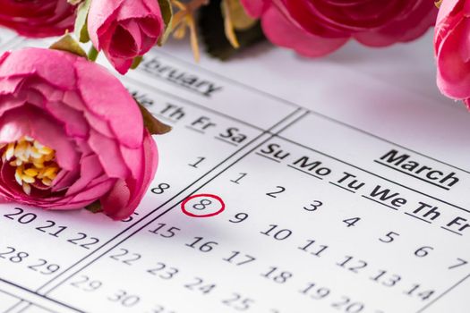 Date on the calendar for Women's Day and flowers. Calendar Reminder - Women's Day March 8th. Date in a red circle closeup on a background of flowers. Selective focus