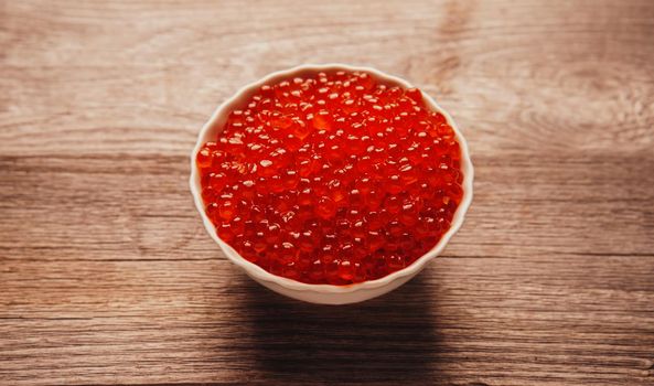 Red salmon caviar in a bowl on wooden background