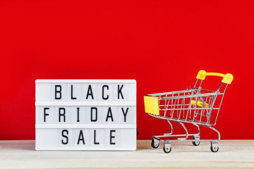 Black Friday sale concept. Mini shopping cart and sign on a red background. Banner for advertising.