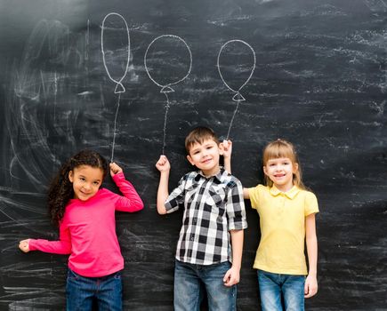 three joyful laughing children keep imaginary balloons drawn on the chalky blackboard
