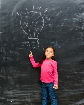 cute little girl pointing on a drawn lamp on chalky blackboard