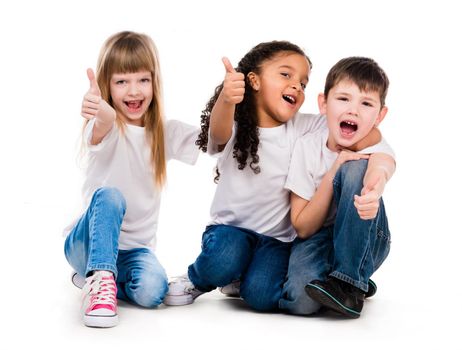 three funny children sitting on the floor with thumbs up isolated on white background