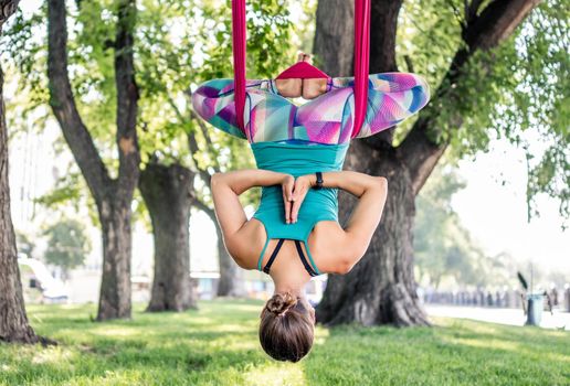 Sport girl practicing fly yoga in hammock at nature and stretching her body. Athlete woman during aero gymnastics outdoors