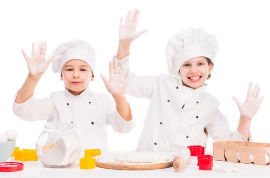 little joyful cooks in uniform making dough with hands up and flour on faces