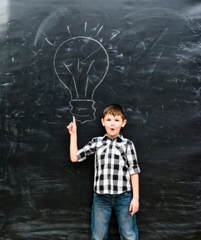 cute little boy with finger up having an idea with drawn lamp on chalky blackboard
