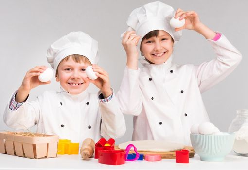 smiling little boy and girl in cook form make dough holding eggs