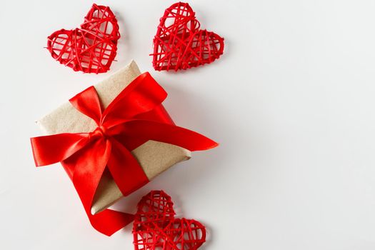 Valentine's day gift and red hearts on a white background. Holiday background for Valentine's day - a gift with a red satin ribbon and handmade hearts on a white background, photo for design.