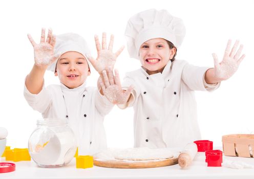 little joyful cooks in uniform making dough with hands up and flour on faces