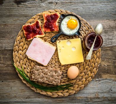english breakfast with cheese, ham, white and grey bread and jam on wooden background