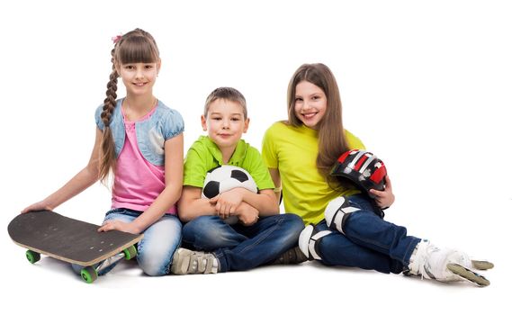 three cute playful children sitting on the floor with sport equipment isolated on white background