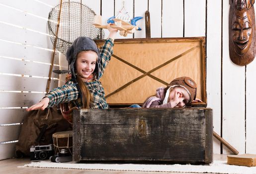 two playful little girls pretending pilots in old big wooden chest