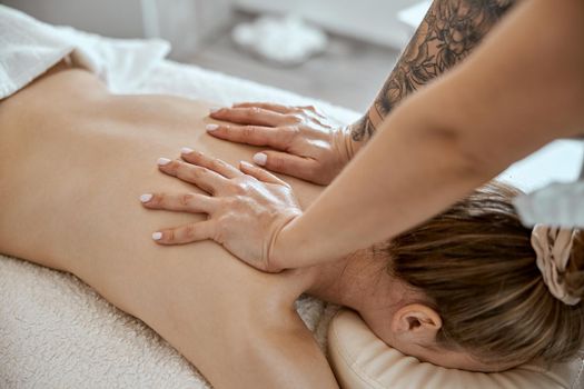 Professional confident massage master is doing procedures to caucasian woman in minimalistic modern cabinet