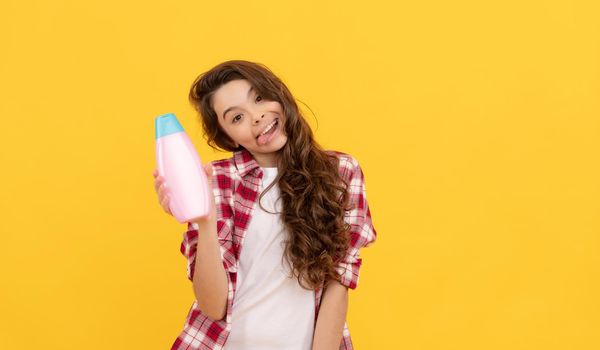 happy teen girl with long curly hair hold shampoo bottle, presenting product.