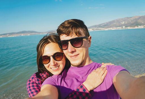 Happy young couple in love taking photographs self-portrait on beach on background of blue sea