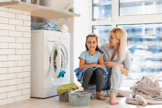 Young housewife and little girl doing laundry together