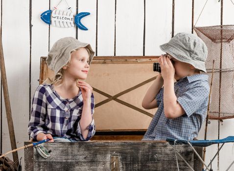 little boy shooting little girl sitting in old big chest