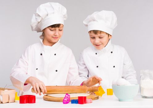 two little cooks in white uniform rolling out a dough in the kitchen
