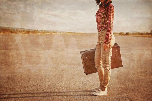 Unrecognizable woman is standing on road with vintage suitcase. Vintage image