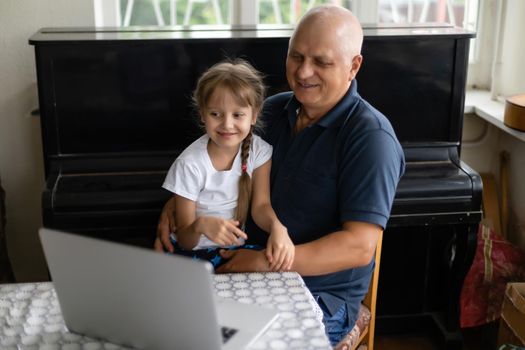 Grandfather and his granddaughter using a laptop together.