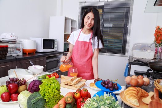 housewife with pouring orange juice jar in kitchen room at home