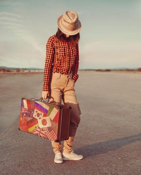 Traveler young woman with a suitcase standing on road. Suitcase with stamps flags of different country