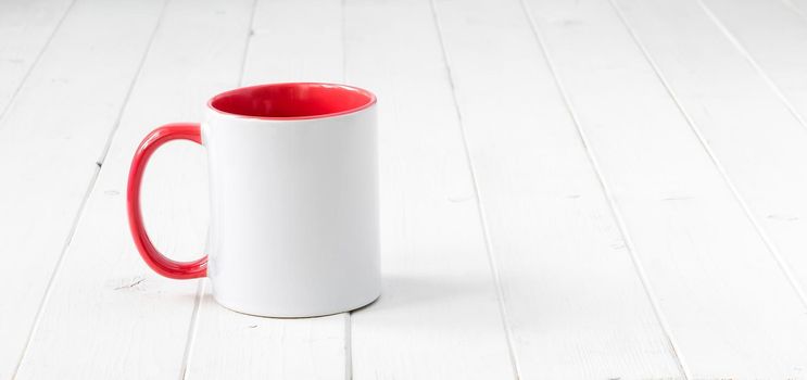 white cup with red handle and inside on white wooden table