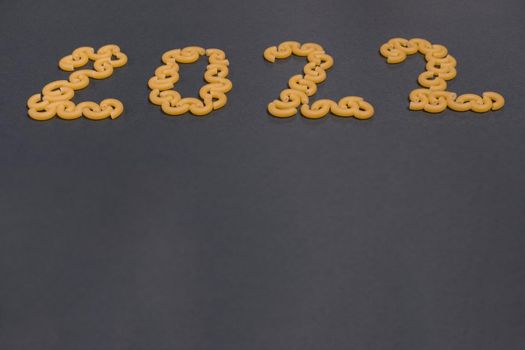 Number 2022 is laid out of pasta on black paper background. Flat lay. Concept photo.