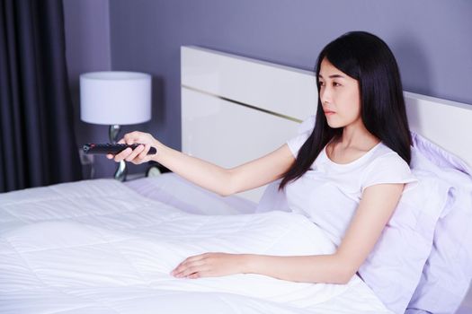 woman watching tv with remote on bed in the bedroom