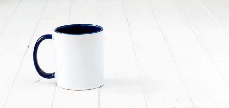 white cup with dark blue handle and inside on white wooden surface