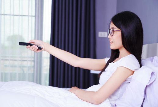 woman watching tv with remote on bed in the bedroom