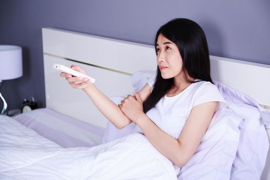 woman feeling cold and hand press remote air conditioner on bed in the bedroom