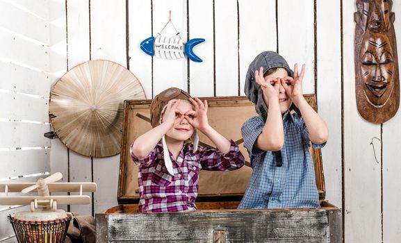 two little kids in pilot hats in big old chest making glasses with hands
