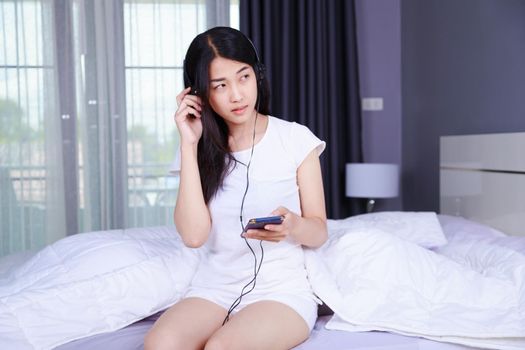 woman in headphones listening to music from smartphone on bed in the bedroom