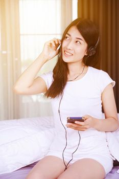 woman in headphones listening to music from smartphone on bed in the bedroom