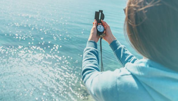 Traveler woman searching direction with a compass on coast near the sea in summer. Rear view