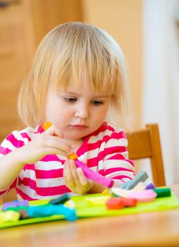 lovely little girl sitting at the table engaged in modeling plasticine